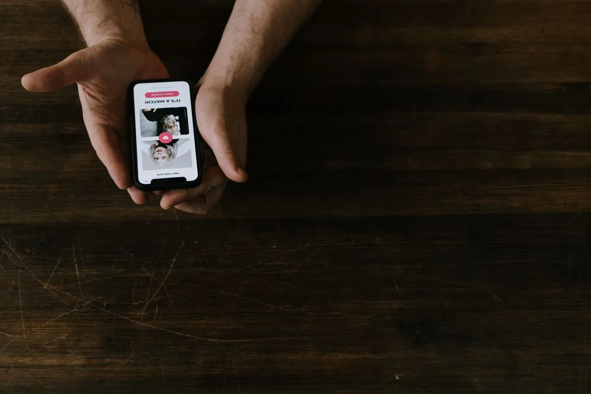 Manos sujetando un smartphone sobre una mesa de madera oscura